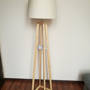 Gaiša priedes koka stāvlampa ar greznu auduma abažūru.