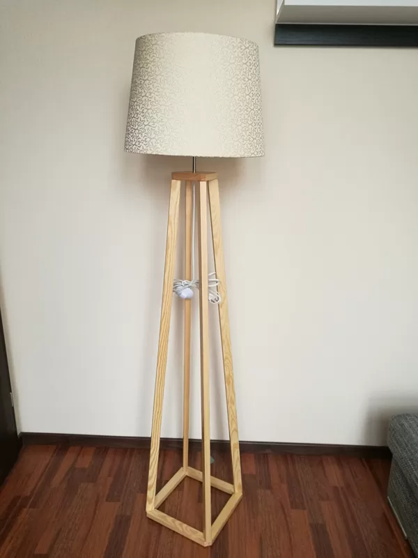 Gaiša priedes koka stāvlampa ar greznu auduma abažūru.